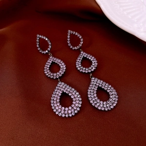 Macro shot of triple-layered teardrop earrings with purple rhinestones on brown silk