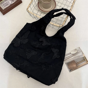 Detailed close-up of a black canvas tote bag featuring decorative lace butterfly appliques
