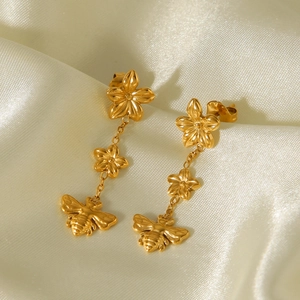 Close-up of golden long drop earrings featuring intricate flower and honey bee charms