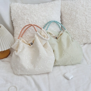 Detail of floral daisy embroidery and woven rope handles on canvas tote bags
