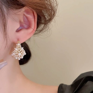 Close-up of geometric gold-plated earrings with diamond-shaped pearl inlay on a model