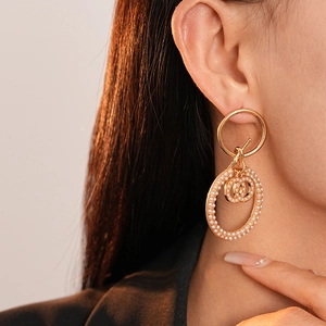 Close-up of golden interlocking CC logo earrings with pearls worn by a model