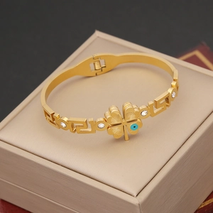Bracciale vintage dorato con quadrifoglio, occhio blu e motivo greco su portagioie beige