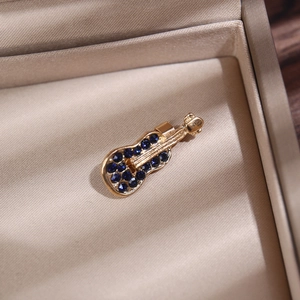 Gros plan d'une broche violon dorée avec strass bleus dans son écrin à bijoux beige texturé