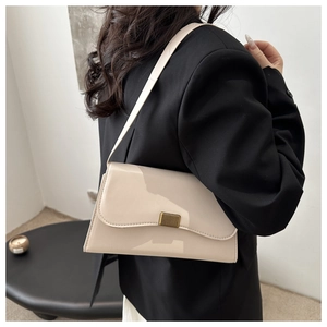 Close-up of a cream patent leather underarm bag featuring a gold textured metal clasp