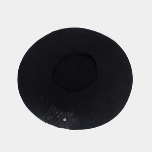 Detail of a black knit beret featuring lace flower patterns and rhinestone accents