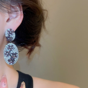 Detailed view of floral zircon stud earrings with purple accents on a model's ear