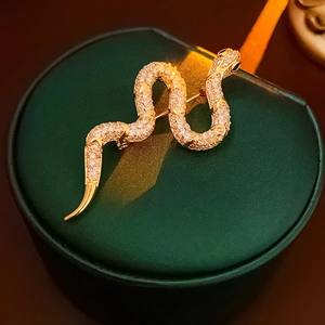 Detailed close-up of a vintage golden snake brooch with white crystals on green velvet box