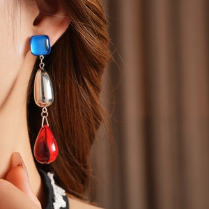 Detail of artistic silver drop earrings with blue square and red waterdrop glass elements