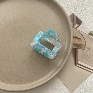 Dettaglio molletta per capelli quadrata con motivo marmorizzato blu su piatto ceramica