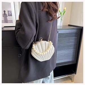 Detailed shot of a white glitter shell bag with pearl handle and gold chain on a black blazer
