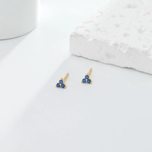 Detail of minimalist gold triangle stud earrings with three round blue gemstones
