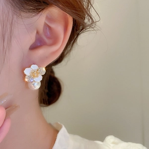 Detail shot of a model wearing zircon flower earrings with white enamel and a pearl drop