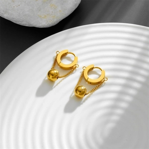Minimalist gold chain ball drop hoop earrings on a textured plate with artistic shadows