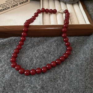 Macro detail of deep red glass beads and silver clasp on a minimalist necklace
