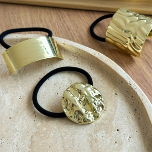 Detail of irregular textured gold metal hair ties on a ceramic plate with black elastic