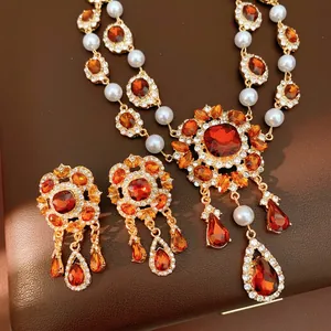 Vintage jewelry set with orange gemstones, pearls, and diamonds on a gold necklace and earrings