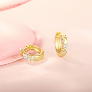 Macro detail of gold huggie earrings with sparkling stardust zircon inlay on pink backdrop