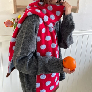 Red plush knit scarf with grey polka dots worn by a model in a cozy indoor setting