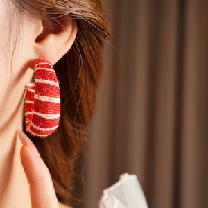 Close-up of model wearing red and white striped woven C-shaped fabric earrings with texture