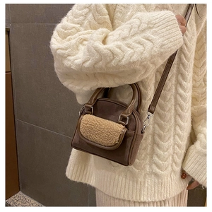 Detail of dark brown suede bag with beige plush pocket and crossbody strap on white sweater