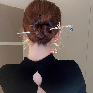 Detail of silver sword hair pin with diamonds and a blue teardrop pendant in a bun