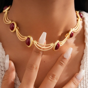 Gros plan d'un collier géométrique vintage doré avec pierres rouges sur un mannequin