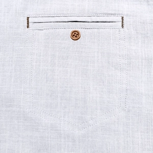 Detail of white cotton linen shirt showing front pocket with a brown wooden button
