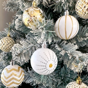 Detail of white and gold Christmas ball ornaments with glitter patterns on a snowy tree
