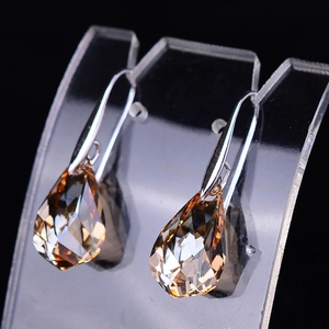 Macro view of teardrop champagne crystal earrings with silver-tone hooks on black background