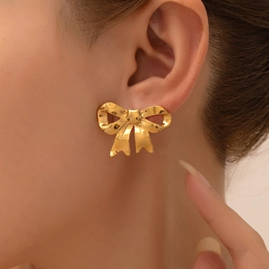 Detailed close-up of golden bow-shaped earrings with vintage hammered metal texture on ear