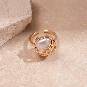 Detailed view of an irregular gold metal ring with a white pearl on a stone surface