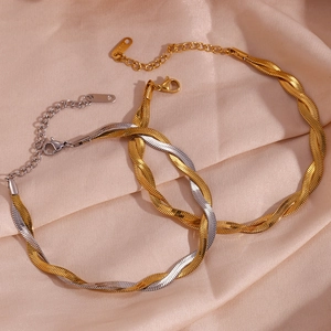 Detailed shot of two-tone braided blade chain anklets on champagne silk fabric background