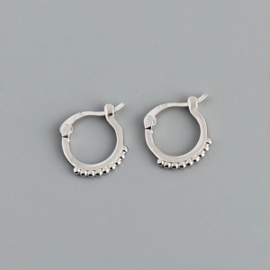 Detail view of silver round hoop earrings with delicate beaded textures on a grey background