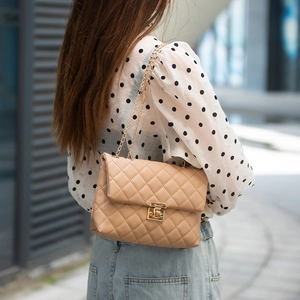 Fashionable beige quilted crossbody bag with gold chain strap shown in urban street style