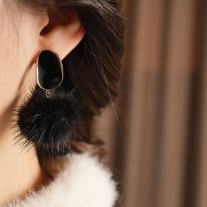 Close-up of black enamel oval stud and fluffy fur pompom drop earring on a model