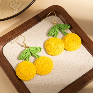 Detail of handmade woven cherry earrings in yellow and green on a wooden tray