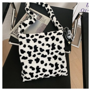 Detail view of cow pattern plush shoulder bag with decorative shoe charm on a black chair