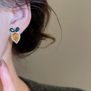 Detailed view of carrot-shaped gold stud earring with orange gem and green leaves