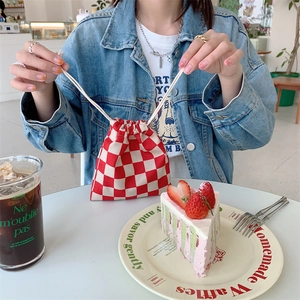 Detalle de una bolsa de lona a cuadros rojos y blancos con cordón llevada por modelo