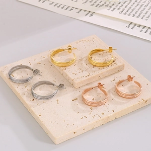 Macro view of C-shaped textured earrings in gold, silver, and rose gold on stone