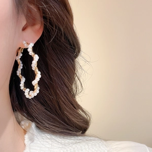 Close-up of elegant gold hoop earrings with white pearls on model in soft warm lighting