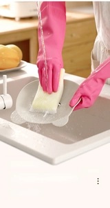 Pink latex cleaning gloves with extended cuffs washing a white plate in a kitchen sink