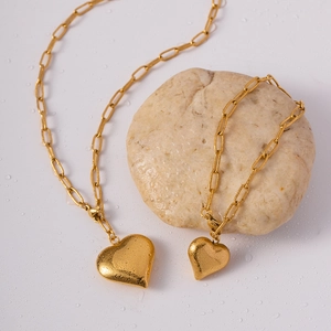Gold stainless steel heart pendant necklace with paperclip chain on wet stones