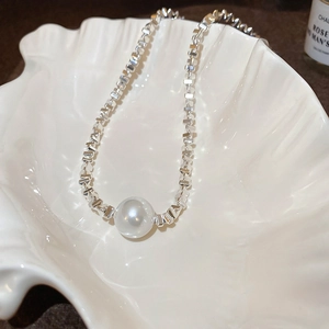 Macro detail of high-luster pearl on a geometric silver chain over shell tray
