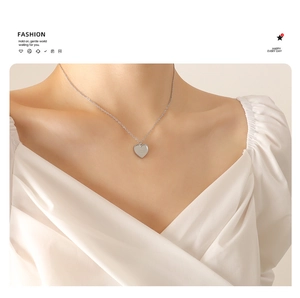 Gros plan d'un collier avec pendentif cœur argenté et gravure porté par un mannequin