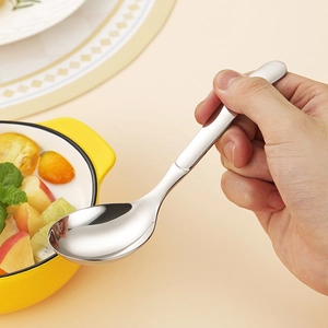 Polished silver 316 stainless steel soup spoon held over a minimalist dining table