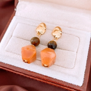 Detail of beaded resin earrings featuring gold metal, brown beads and orange pendants