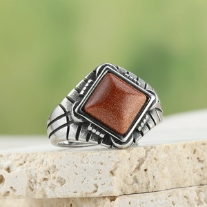 Macro detail of men's vintage stainless steel ring with square red sandstone and carvings