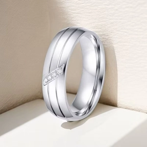 Polished titanium steel ring with parallel grooves and inlaid diamonds on a beige background
